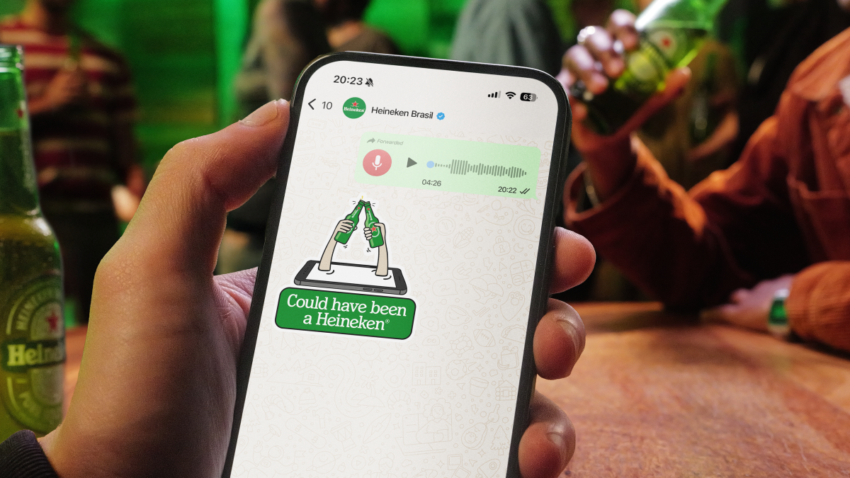 A hand holding a phone displaying a 'Could have been a Heineken' sticker received on WhatsApp after sending a long voice message.