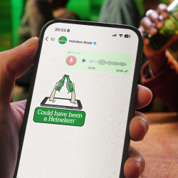 A hand holding a phone displaying a 'Could have been a Heineken' sticker received on WhatsApp after sending a long voice message.