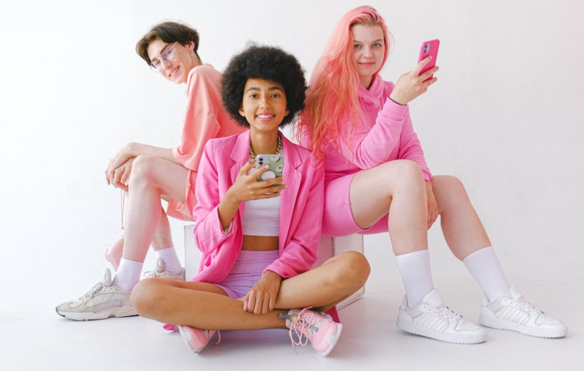 Three young people all wearing bright pink, two of them using smartphones.