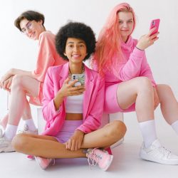 Three young people all wearing bright pink, two of them using smartphones.