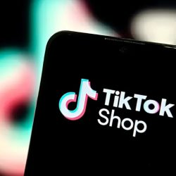 A phone open to TikTok Shop, held in front of the TikTok logo.
